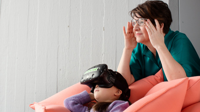 Aikuinen ja lapsi katsovat samaan suuntaa, lapsella on VR-lasit päässään.