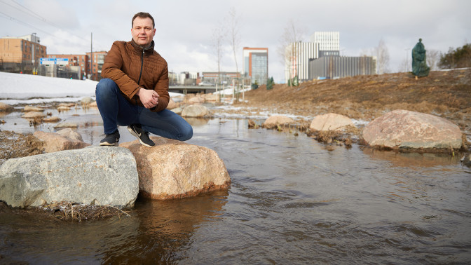 Harri on kyykyssä kivellä kaupunkipuron rannalla.