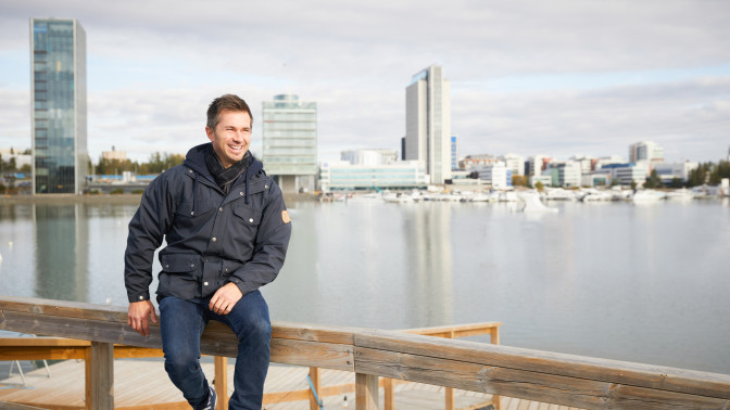 Tuomas Lukkari istuu kaiteella kaupunkimaiseman edessä.