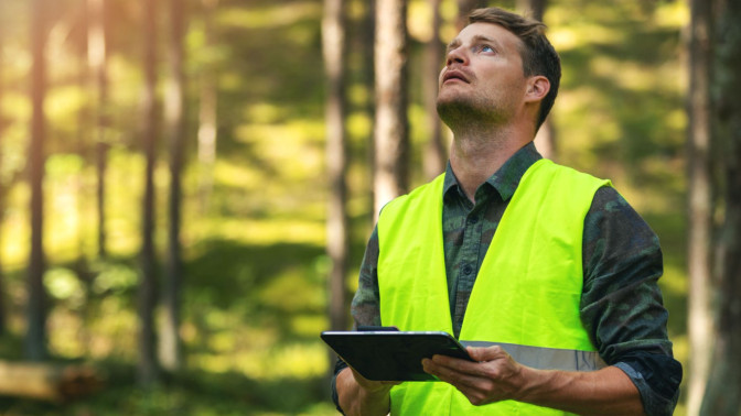 Mies huomioliivissä metsässä tablettitietokone käsissään
