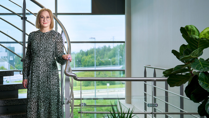 Anne Mikkola seisoo portaikossa toimistolla lasiseinän edessä.