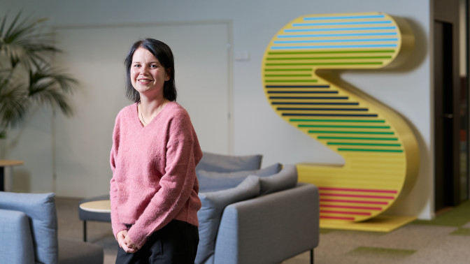 Emma Liljeström seisoo toimiston aulassa ja hymyilee kameralle.