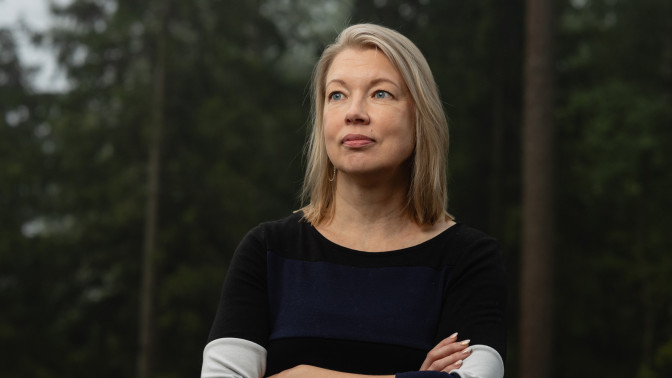 Nora Sillanpää seisoo metsän edustalla luoden rauhallisen katseen kameran ohi.