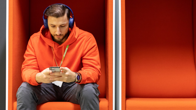 Henkilö istuu yksin oranssissa puhelinkopissa ja tutkii puhelintaan.