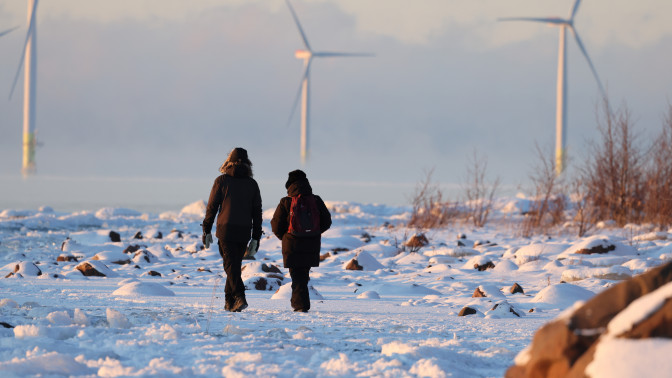 Kaksi ihmistä kävelee lumisella rannalla.