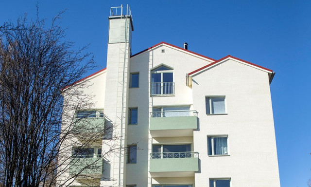 As Oy Kauppaneuvoksentie 4:n peruskorjattu valkoinen julkisivu kokonaisuudessaan auringonpaisteessa.