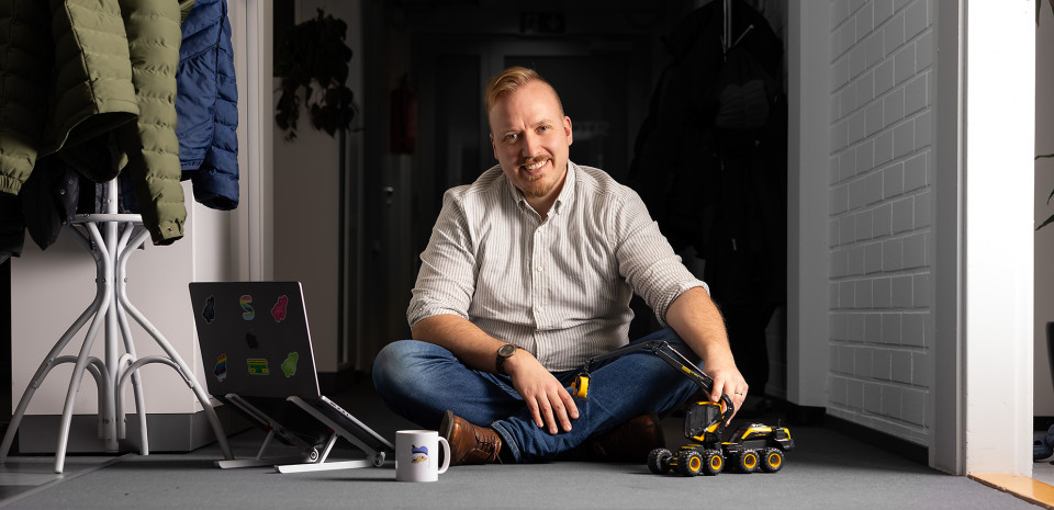 Miika Hakala istuu lattialla tietokoneen, kahvimukin ja lelumoton kanssa.