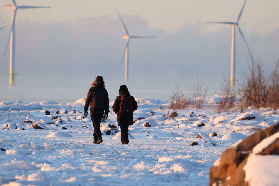 Kaksi ihmistä kävelee lumisella rannalla.