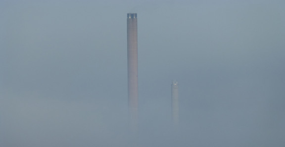 Teollisuuslaitoksen savupiiput sumussa.