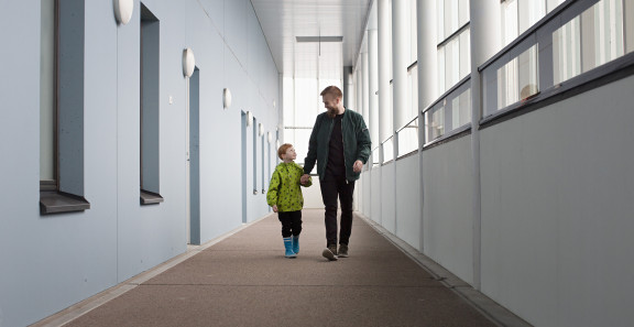 Mies ja lapsi kävelevät kerrostalon käytävällä.