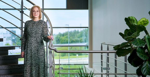 Anne Mikkola seisoo portaikossa toimistolla lasiseinän edessä.