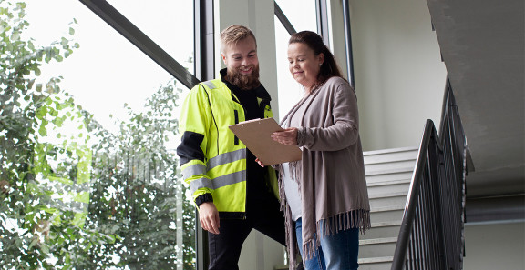 Kaksi henkilöä tarkastelee dokumenttia portaikossa työmaaympäristössä
