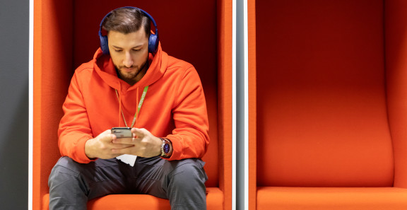Henkilö istuu yksin oranssissa puhelinkopissa ja tutkii puhelintaan.