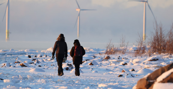 Kaksi ihmistä kävelee lumisella rannalla.
