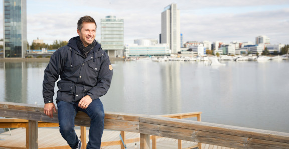 Sitowisen Tuomas Lukkari istuu aidalla kaupunkimaisemissa.