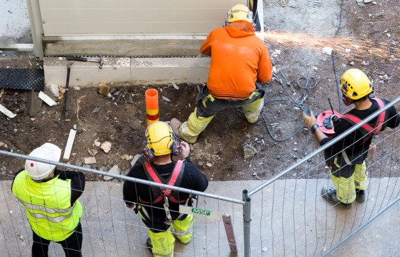 Suunnittelija ja urakoitsijan edustajat rakennuksen pihalla.