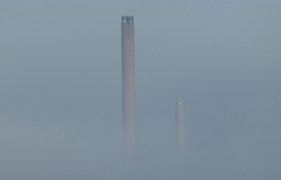 Teollisuuslaitoksen savupiiput sumussa.