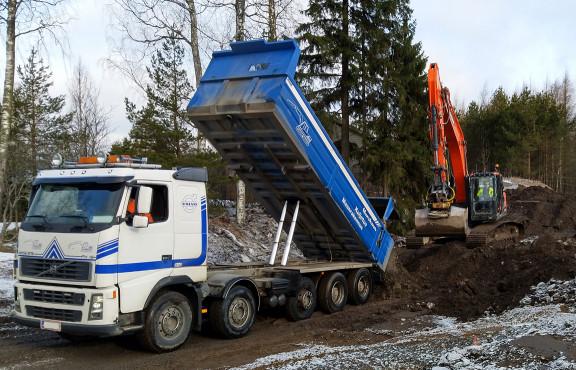 Kuorma-auto kaataa maamassat kaivinkoneen eteen.