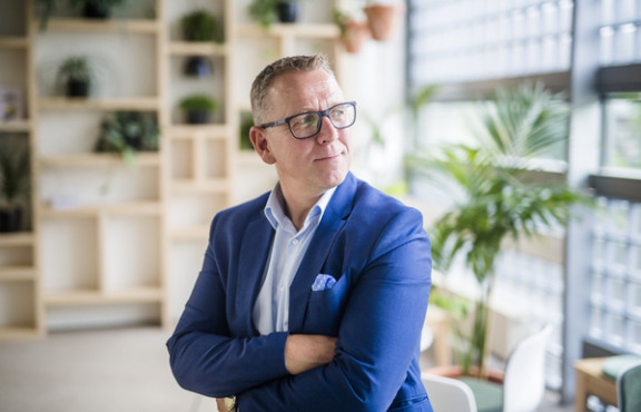 Jyri Arponen nojaa pöytään ja katsoo ikkunasta ulos.