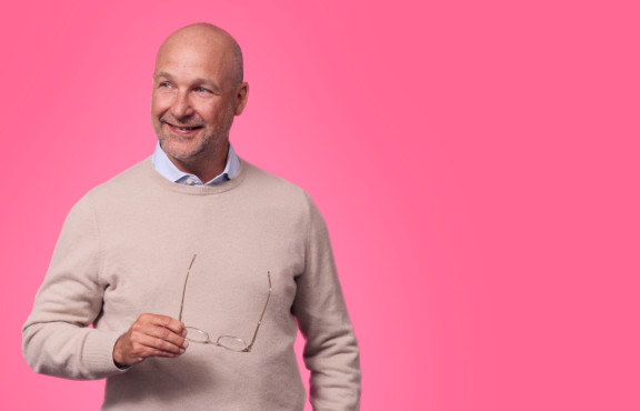 mies hymyilee kuvassa ja pitää silmälaseja