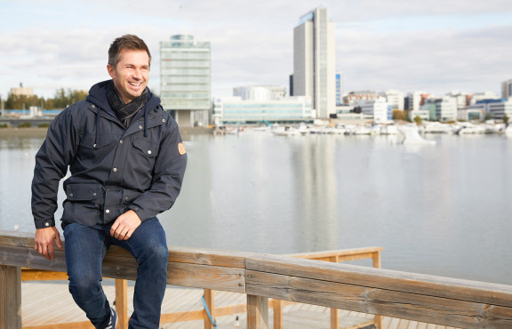 Sitowisen Tuomas Lukkari istuu aidalla kaupunkimaisemissa.