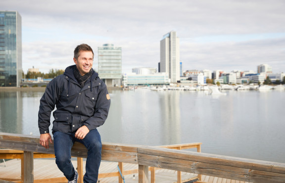 Henkilö istuu terassikaiteella kaupunkiympäristössä rakennusten edustalla.