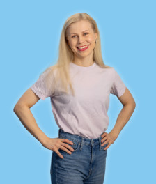 Henkilö seisoo kädet lanteilla vaaleassa T-paidassa ja farkuissa sinistä taustaa vasten