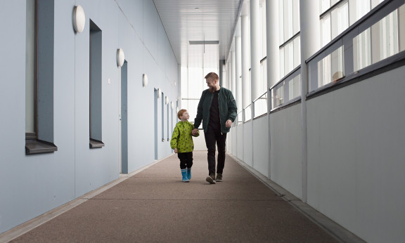 Mies ja lapsi kävelevät kerrostalon käytävällä.