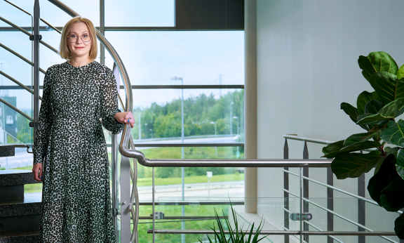 Anne Mikkola seisoo portaikossa toimistolla lasiseinän edessä.