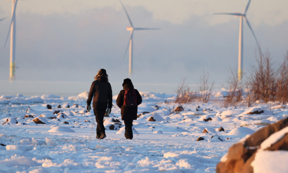 Kaksi ihmistä kävelee lumisella rannalla.