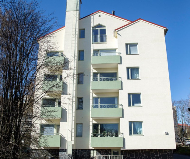 As Oy Kauppaneuvoksentie 4:n peruskorjattu valkoinen julkisivu kokonaisuudessaan auringonpaisteessa.